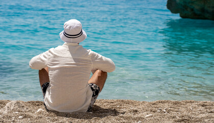 Fototapeta na wymiar Holiday on the beach. Back view of relaxed young man in white shirt enjoying sea view 