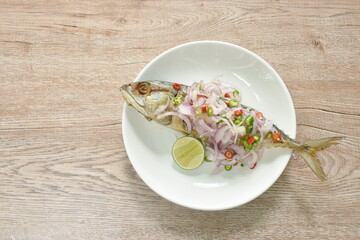 deep fried salty mackerel fish topping chop shallot and chili with slice lemon on plate