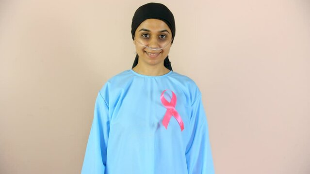 An attractive woman putting a pink ribbon on her chest supporting breast cancer - Breast Cancer Awareness. A young cancer patient in a black headscarf smiling while looking at the camera - cheerful...