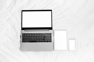 laptop, tablet and phone with white blank screen on a white bed