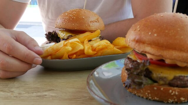 View on rench fries next to a huge cheeseburger or burger with a cutlet, lettuce, cheese and tomatoes inside. Unhealthy, fatty food on the street in a summer restaurant