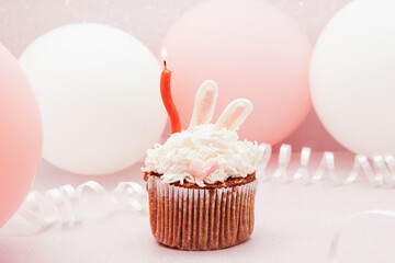 Bunny cupcake and red candle on glitter pink background with air balloons, happy birthday card