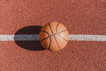 Old orange ball for basketball lying on the rubber sport court.Sport red ground outdoor in the...