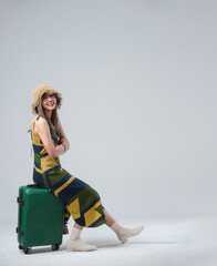 Happy Asian woman traveler siting and holding suitcase isolated on gray background, Tourist girl...