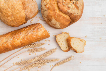 Fresh white wheat bread, round classic, ciabatta, french baguette, wheat ears and grains on white wooden background top view. Bread making, bakery, healthy food. Bread background. Light mockup