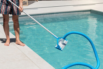 Unrecognizable man cleaning the swimming pool with an automatic pool cleaner at his house backyard