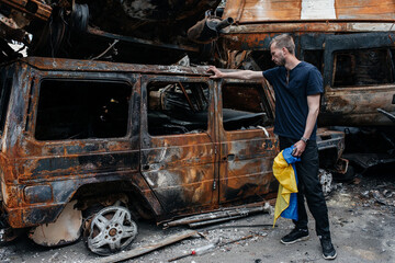 Man with Ukrainian flag stands against cars cemetery in Irpin. Consequences of the Russian military...