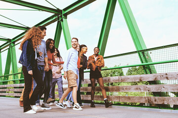 a group of multiracial young people walking together crossing a bridge on a weekend day - lifestyle concept of friendship, brotherhood between different cultures, integration and internationalization