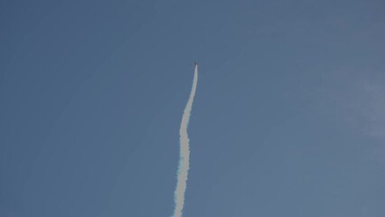 A demonstrations of a sports plane is rising straight into the sky and emitting smoke.