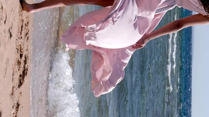 Woman hand holding pink dress on a windy day on a beach with sea as background.