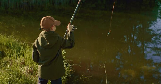 schooler boy is fishing in early morning, casting rod and waiting for bite, 4K, Prores