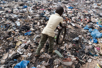 Top view of a small African boy playing with an old bike tire in a heavily polluted area; symbol of...