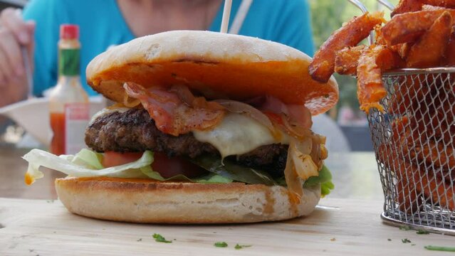 View on rench fries next to a huge cheeseburger or burger with a cutlet, lettuce, cheese and tomatoes inside. Unhealthy, fatty food on the street in a summer restaurant