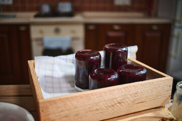 Jars with berry jam stacking upside down on wooden crate, standing on kitchen island