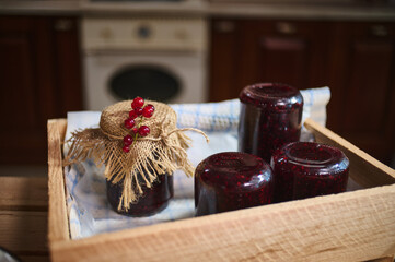 Berry jam in jars stacked upside down on crate and bottle of jelly ornate with burlap and red...