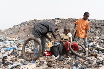 Three homeless street boys in a landfill with their daily loot of garbage to recycle and sell; condition of slum children in Africa - obrazy, fototapety, plakaty