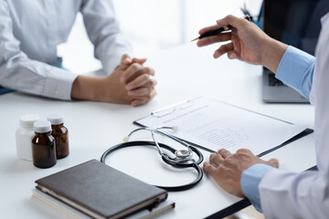 Doctor and patient sitting and talking at medical examination at hospital office, close-up. Therapist filling up medication history records. Medicine and healthcare concept.