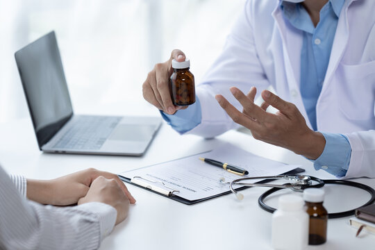 Doctor and patient sitting and talking at medical examination at hospital office, close-up. Therapist filling up medication history records. Medicine and healthcare concept.