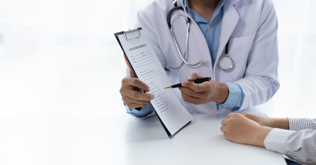 Doctor and patient sitting and talking at medical examination at hospital office, close-up. Therapist filling up medication history records. Medicine and healthcare concept.