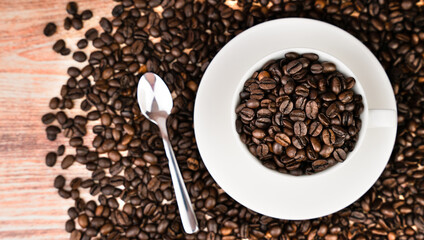 Aromatic coffee beans in a white cup and spoon on a coffee background. Top view. Selective focus.