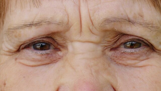 Brown eyes of senior retired woman looking closely to camera. Aged skin with wrinkles of elderly caucasian lady. Face of female old model, grandmother, pensioner. Front view. Close up