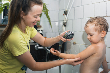 Mom washes her son in the shower in the bathroom with a joyful smile