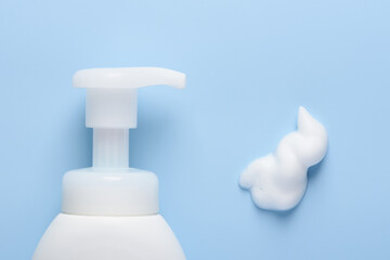 White cosmetic bottle with pump dispenser and foam smear on blue background top view flat lay