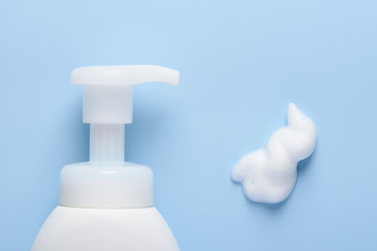 White cosmetic bottle with pump dispenser and foam smear on blue background top view flat lay
