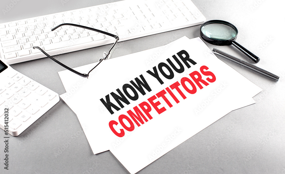 Poster know your competitors text on a paper on a gray background near a calculator and a white keyboard