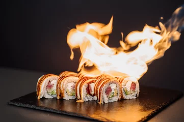 Selbstklebende Fototapeten Preparing of sushi rolls with a fire on black background © rostyslav84