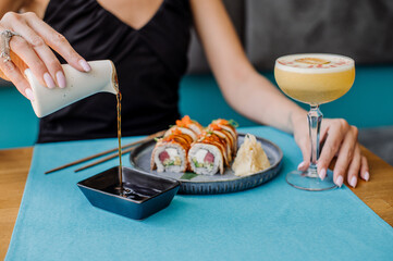 Female client in the restaurant pouring soy sauce and preparing to eat sushi