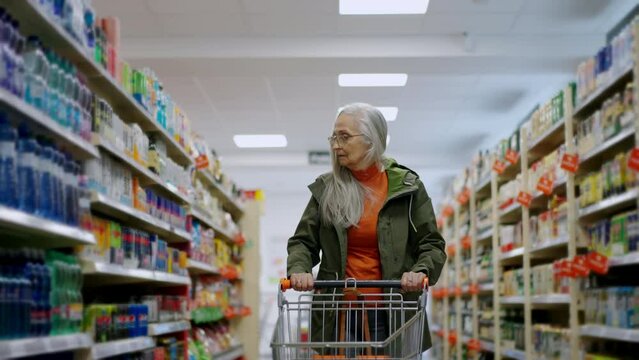 Elder woman walking with empty trolley and shopping in supermarket, inflation and increasing prices concept.
