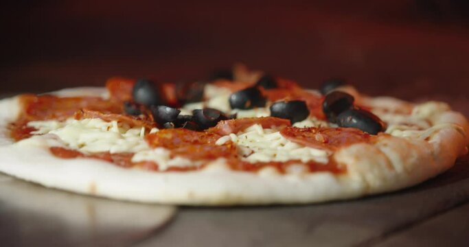 Cooking fresh pizza with olives and salami in a hot wood fired oven