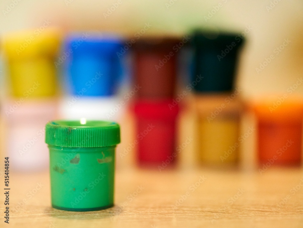 Poster closeup shot of a small green container of watercolor on the table with a blurred background