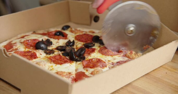 Cutting fresh pizza with olives and salami using a pizza wheel