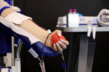 Woman blood donor in chair during donation with a blood bag and red bouncy ball in hand, selective...