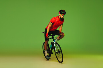 Male cyclist riding bicycle in sports uniform and protective helmet isolated on green studio...