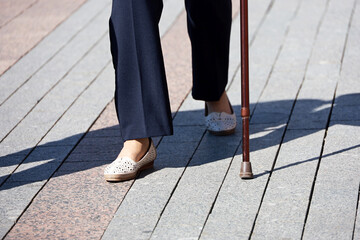 Woman walking with cane on a street, legs in motion on sidewalk. Concept of disability, limping adult, diseases of the spine