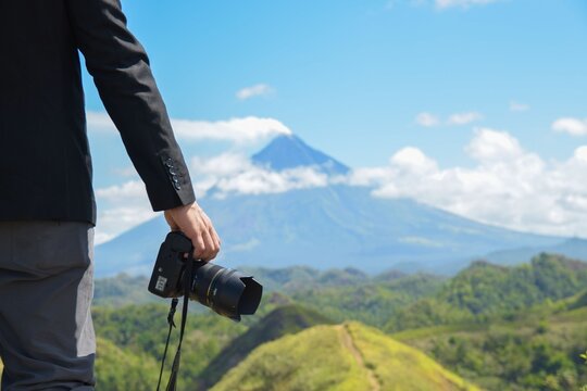 Scenic view of a hand with a camera with Mayon Volcano surrounded by greenery in the background