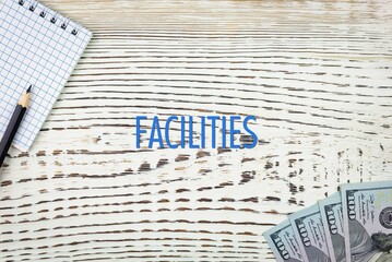 Naklejka premium FACILITIES - word (text) and dollars on a white wooden table, notebook, notepad. Business concept: buying, selling, commerce (copy space).