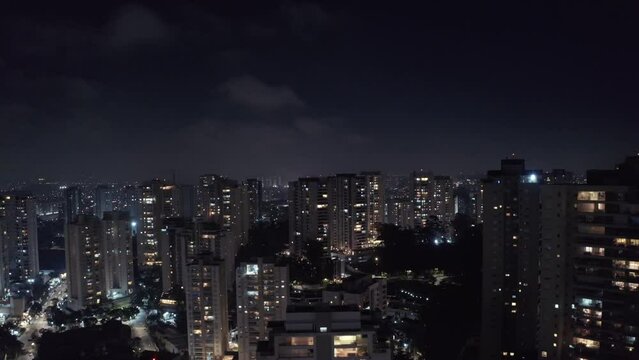 Descending Sao Paulo Morumbi neighborhood lit up at night with downtown cityscape skyline, Aerial Brasil