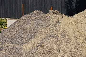 heaps of brown sand and gray rubble on the street by the black wall fence