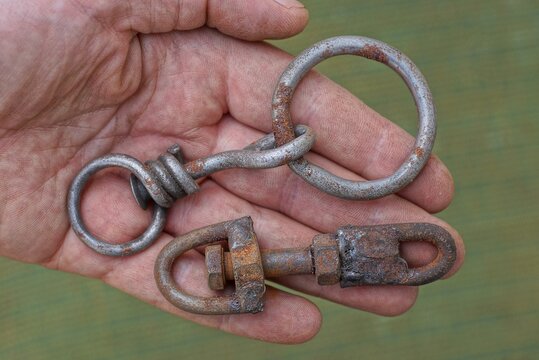 two old rusty metal snap hooks lie on the palm of the hand on a green background