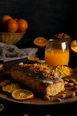 orange cake pudding with almonds and whole and sliced natural oranges and orange juice on a dark table