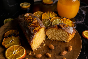 orange cake pudding with almonds and whole and sliced natural oranges and orange juice on a dark table