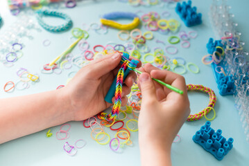 A girl makes a rainbow bracelet from rubber bands crochet. Closeup of making decorative bracelet...