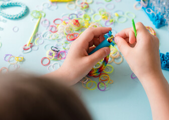 A girl makes a rainbow bracelet from rubber bands crochet. Closeup of making decorative bracelet...