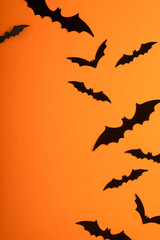 Orange Halloween background. Flock of black bats for Halloween. Black paper bat silhouettes on...