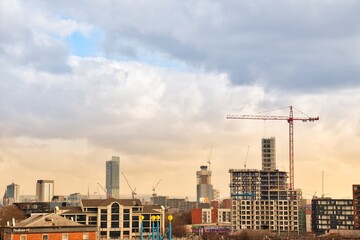 Fototapeta premium City view with modern buildings and construction work with large cranes. Manchester skyline at sunset. 