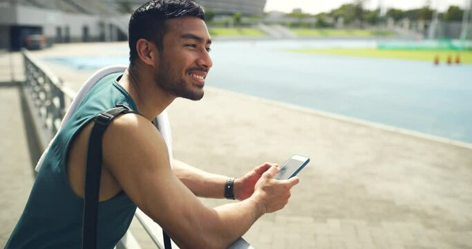 Fit, active, sporty, athletic man updating workout health report on fitness app. Proud athlete texting on phone, thinking and feeling successful after finishing a training exercise in sports stadium.